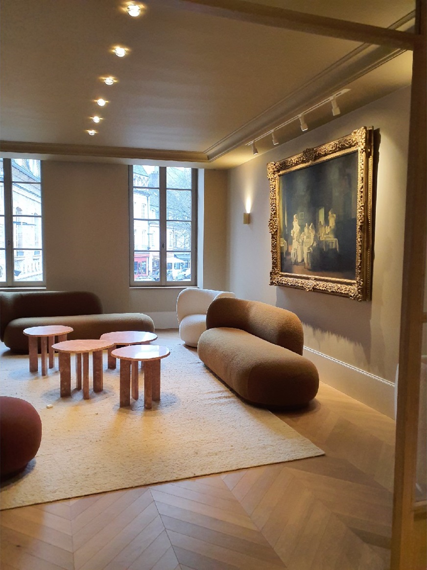 Salon aux canapés bouclés et tables basses en pierre rose, sous un grand tableau à cadre doré
