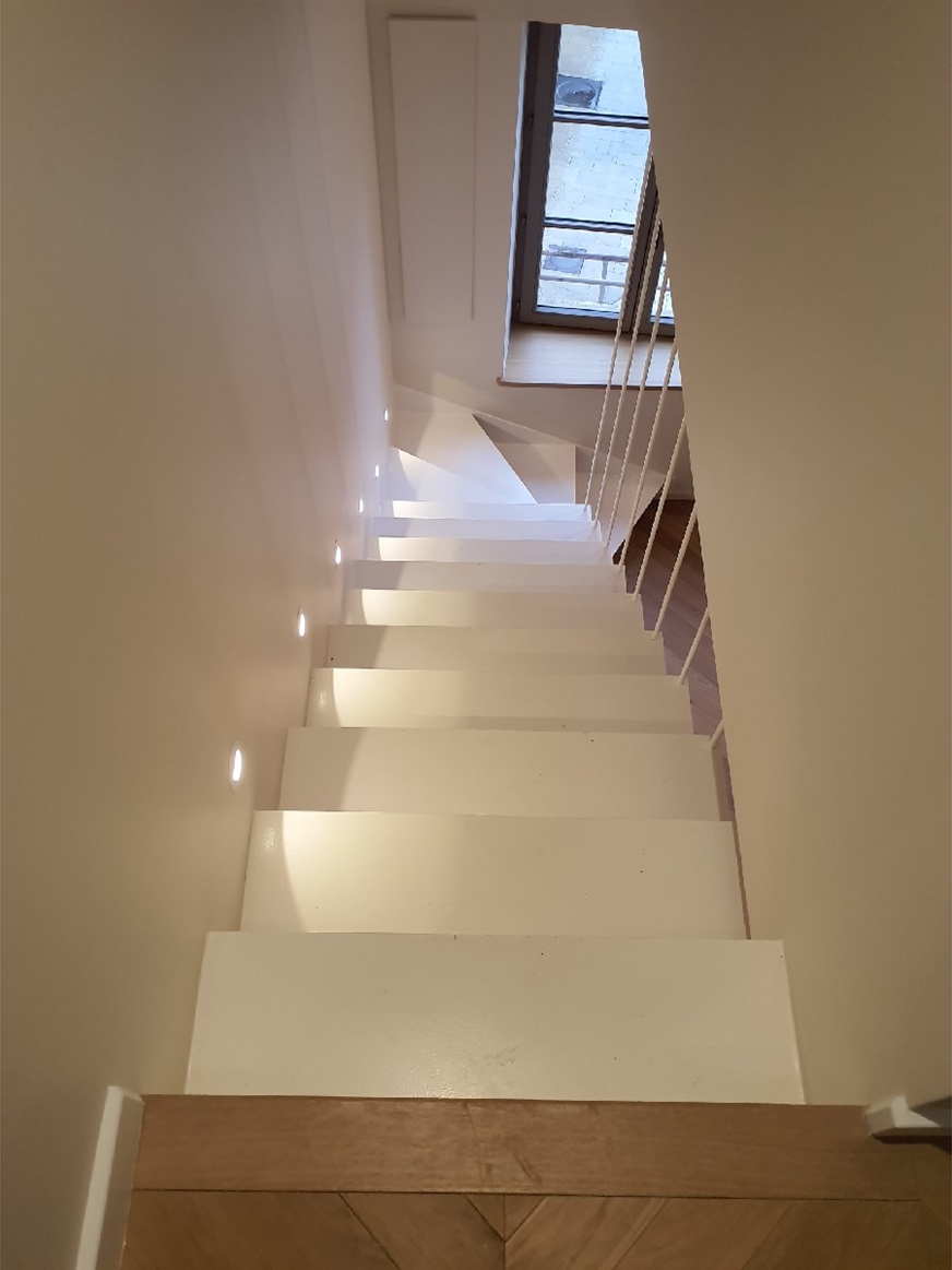 Escalier aux marches blanches éclairé par des spots encastrés dans le mur
