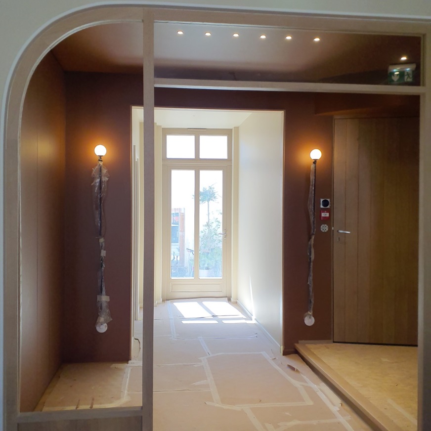 Entrée habillée de bois avec appliques murales et porte-fenêtre, en cours de finition